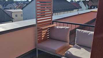 A rooftop terrace with a wooden partition, a cushioned seating area, and a patterned rug.