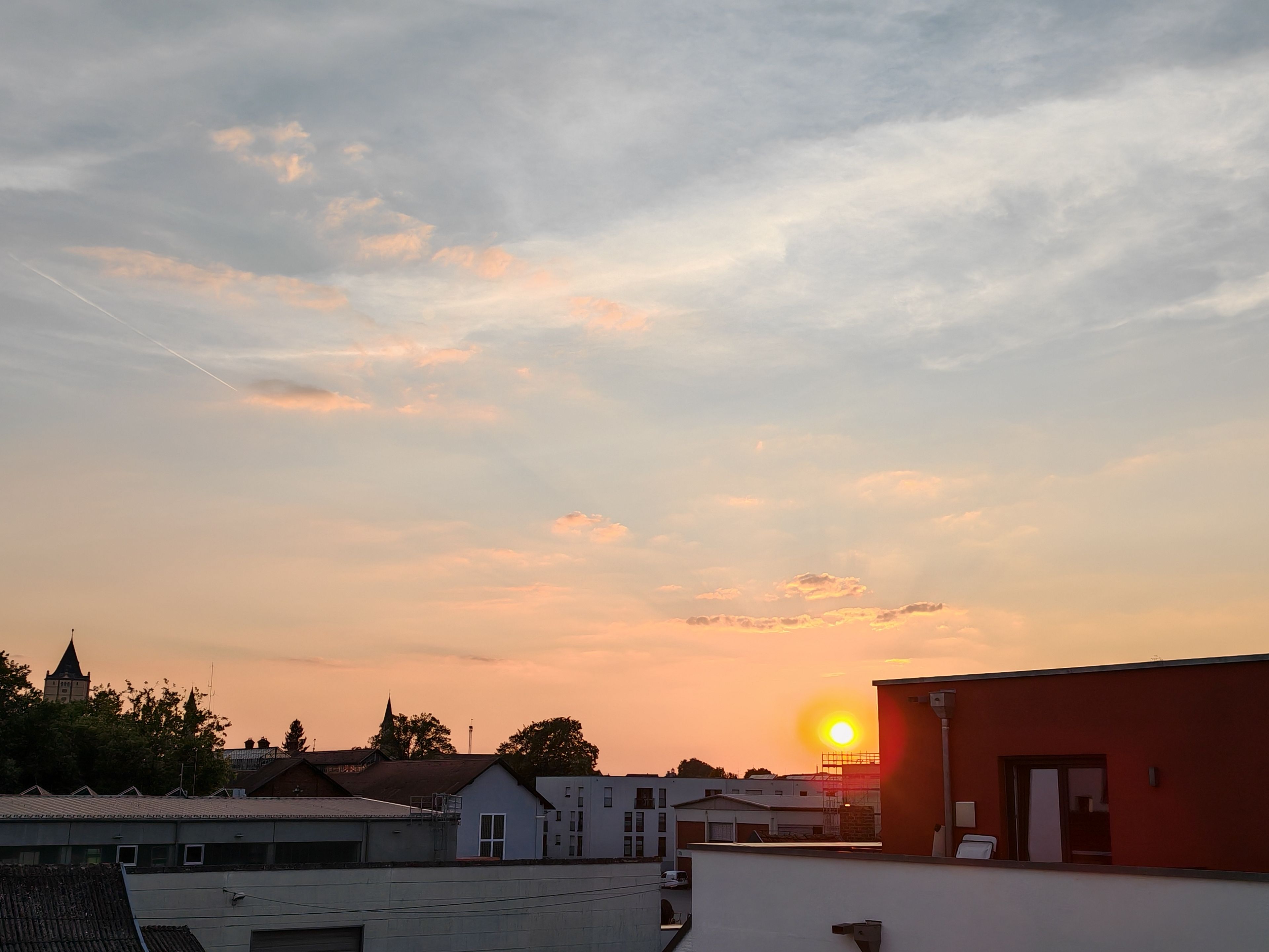 Tramonto su una zona residenziale con edifici e il campanile di una chiesa.