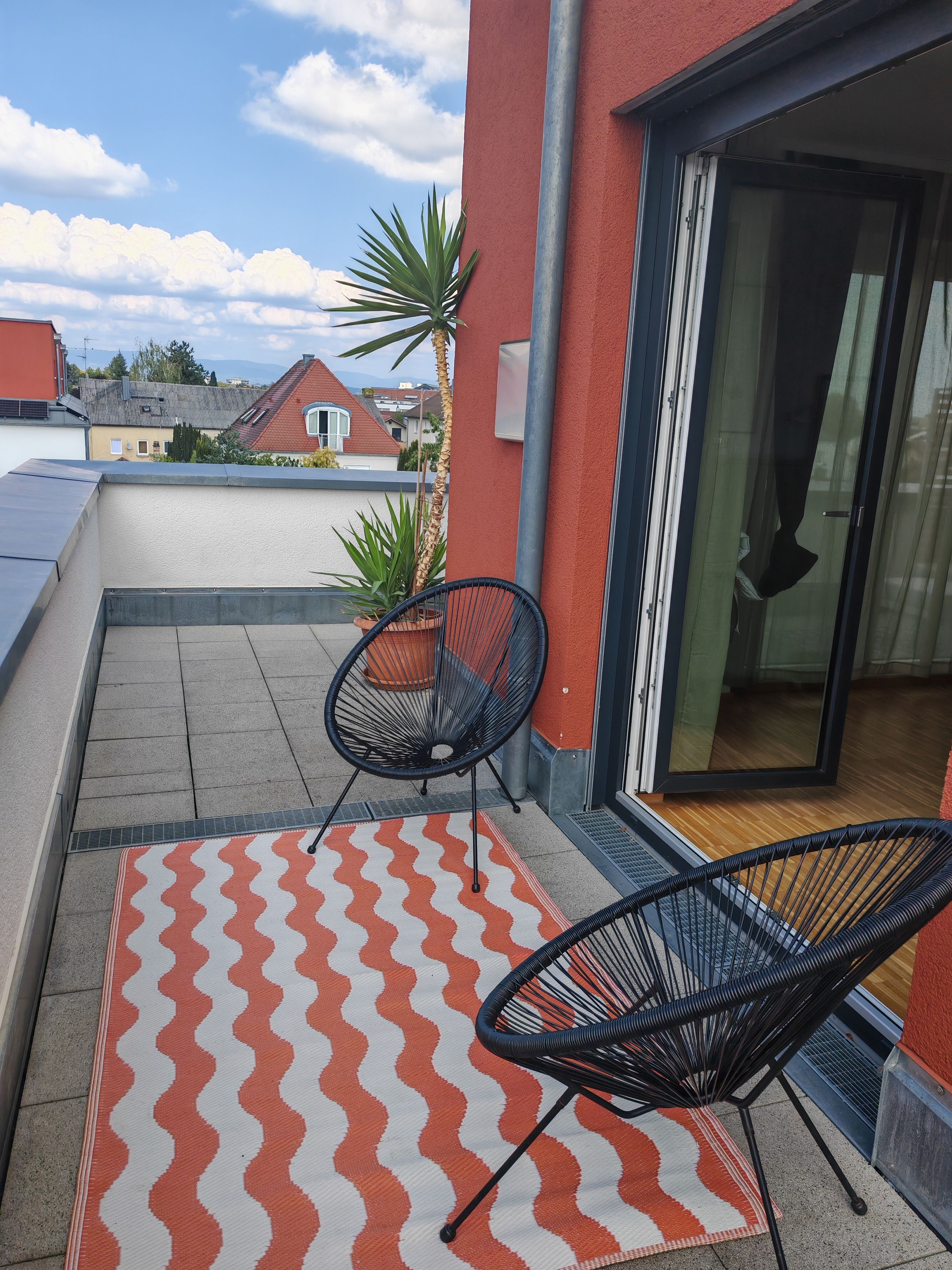 A balcony with two chairs, a patterned rug, and a potted plant.