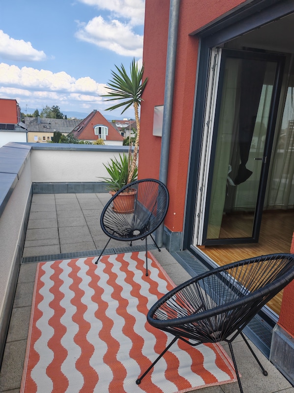 A balcony with two chairs, a patterned rug, and a potted plant.