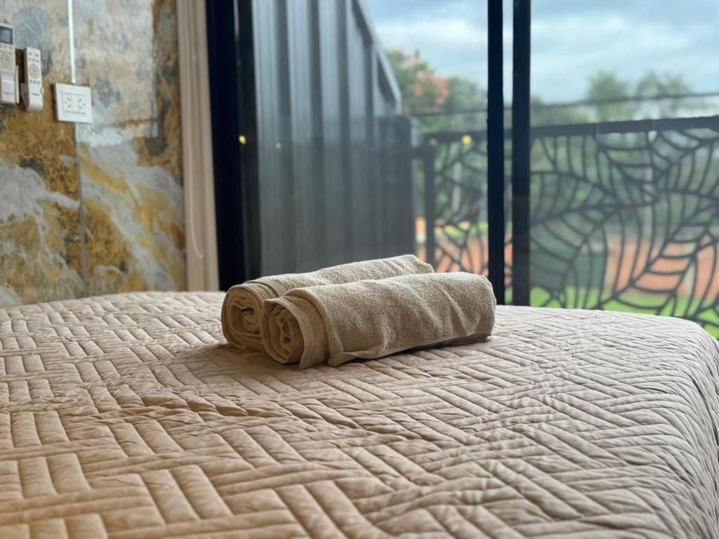 A bed with a rolled towel and a window with a view of greenery.