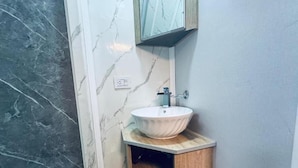 Un bagno con una parete in marmo, un mobiletto contenitore in legno e un lavandino bianco.