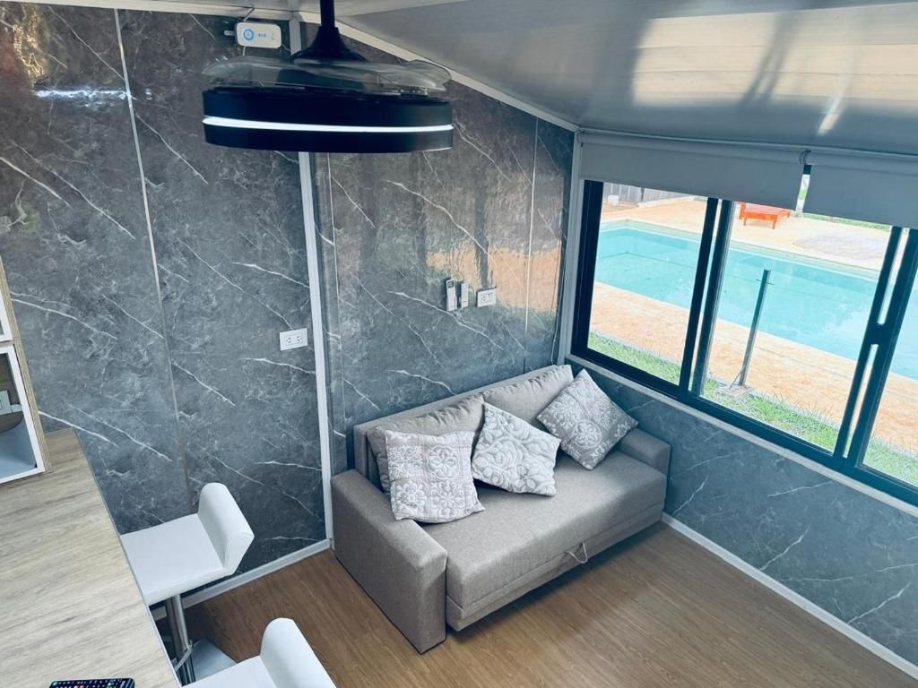 A modern room with a grey sofa, a small table, and a large window offering a view of a pool.