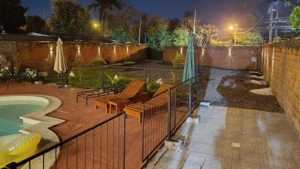 Area piscina con terrazza in legno, poltrone relax e parete in mattoni.