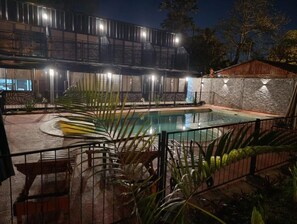 Zona de piscina amb un edifici modern al fons, envoltada de verdura i una paret de pedra.