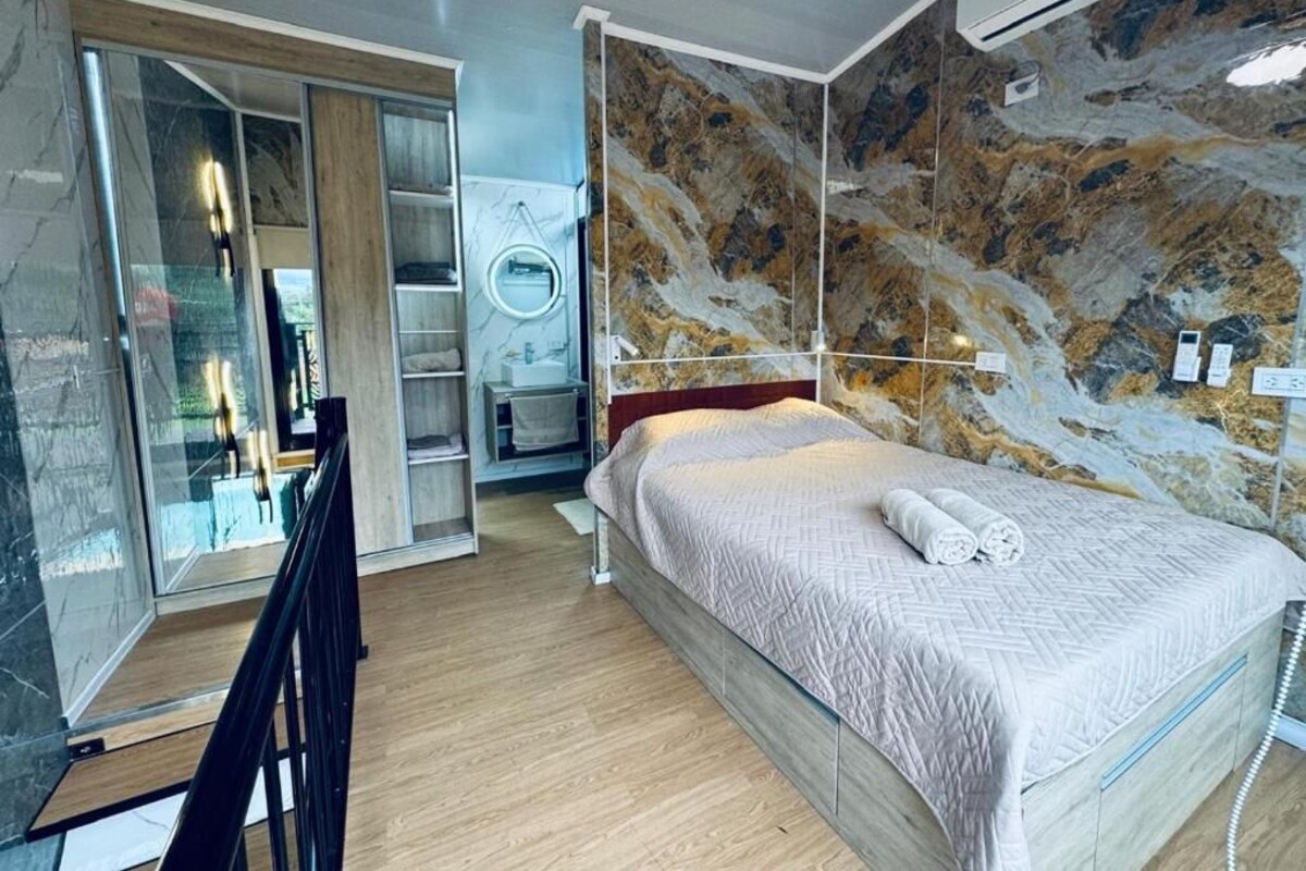 A hotel room with a bed, a mirror, a wardrobe, and a bathroom with a shower.