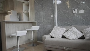 Un soggiorno moderno con un divano grigio, cuscini decorati e uno sgabello da bar bianco.