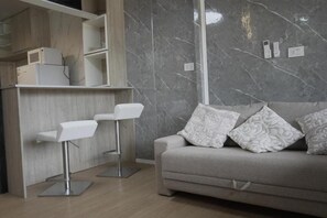 A modern living area with a grey sofa, patterned cushions, and a white bar stool. - Güigüa Apart-Hotel (Puerto Iguazú)
