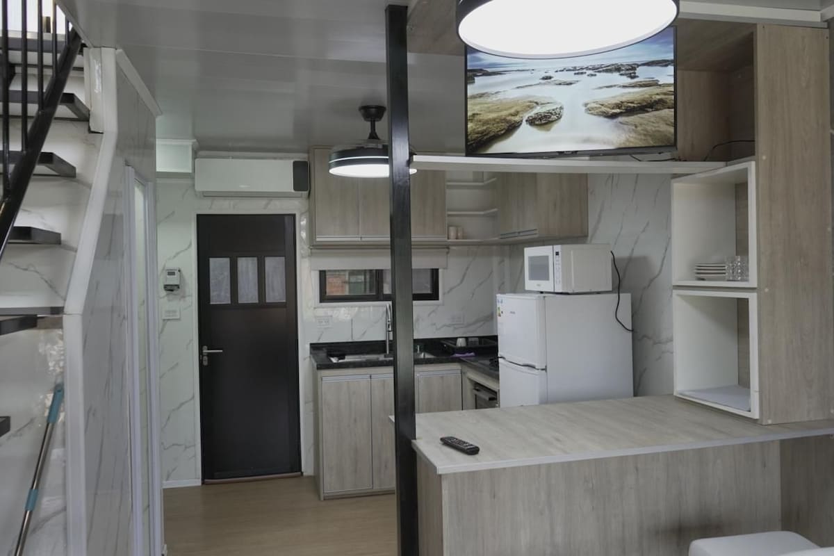 A modern kitchen with a built-in microwave, a refrigerator, and a TV mounted above the counter.