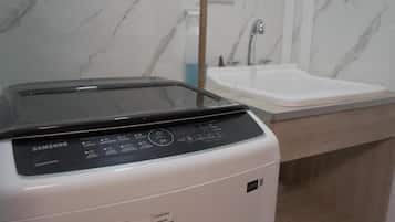 Una lavadora Samsung en un baño con pared de mármol y un lavabo.