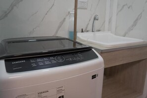 Een Samsung wasmachine in een badkamer met een marmeren wand en een wastafel.
