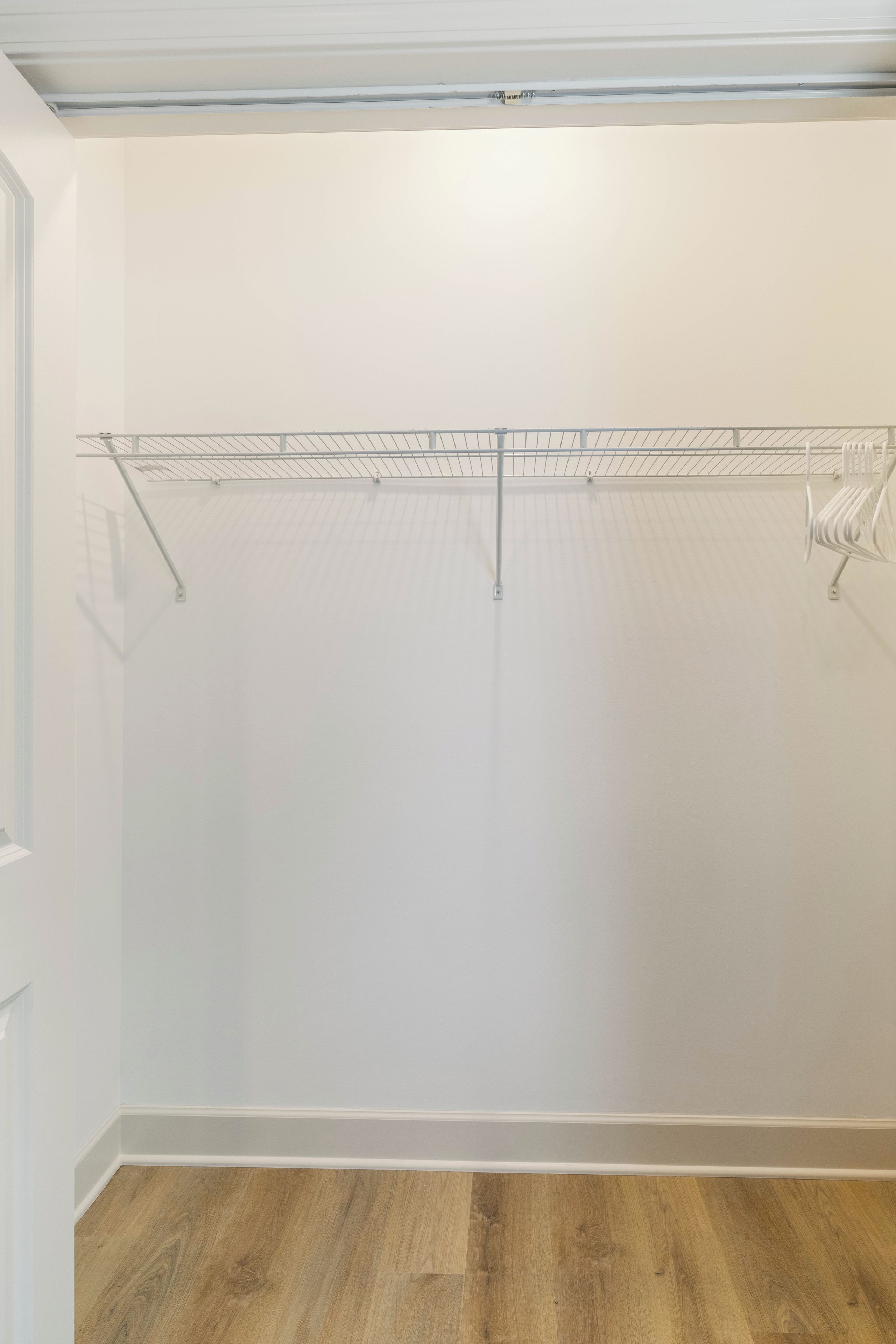 Een kamer met een witte muur, een houten vloer en een metalen rek.
