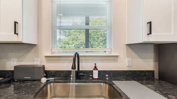A kitchen with a stainless steel sink, a toaster, and a window with blinds.
