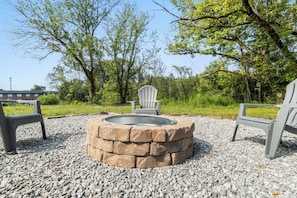 Ein Feuerkorb, umgeben von einer Steinsäule, mit zwei Adirondack-Stühlen an jeder Seite.