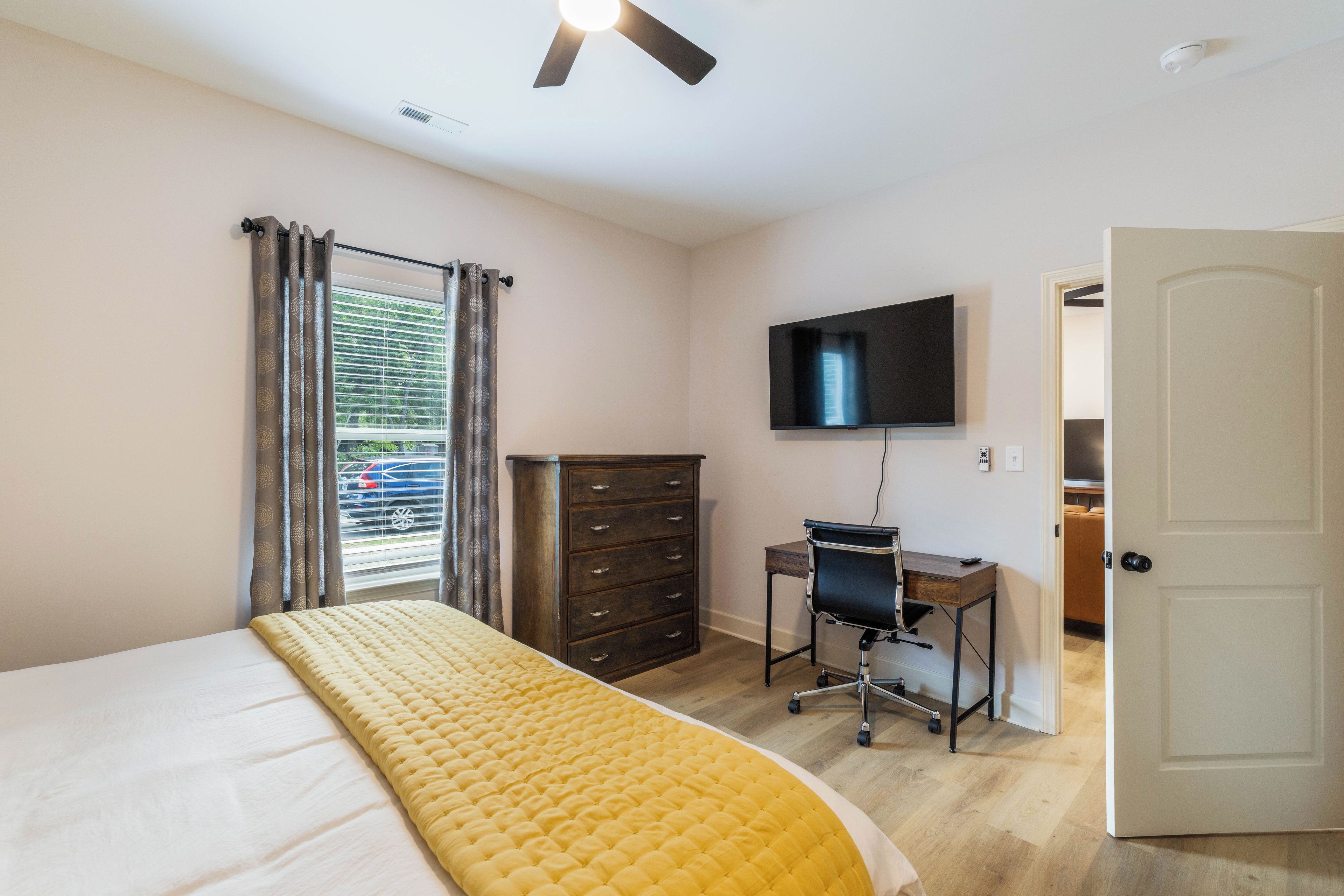 Een slaapkamer met een bed, een bureau, een stoel, een kledingkast, een televisie en een deur.