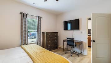 Een slaapkamer met een bed, een bureau, een stoel, een kledingkast, een televisie en een deur.