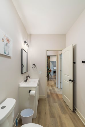 Ein modernes Badezimmer mit Toilette, Waschbecken und Spiegel. Ein Gang führt zu einem Essbereich.
