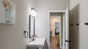 Een moderne badkamer met toilet, wastafel en bidet, een spiegel en een schilderij van bloemen aan de muur.