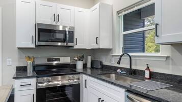 Cozinha moderna com eletrodomésticos de aço inoxidável, armários brancos e piso de madeira.