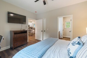 Une chambre à coucher comprenant un lit, une commode, un téléviseur et une porte donnant sur la cuisine.