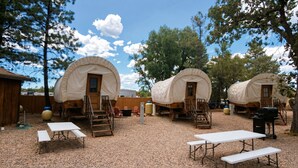 Un camping con carros cubiertos, mesas de picnic y una parrilla.