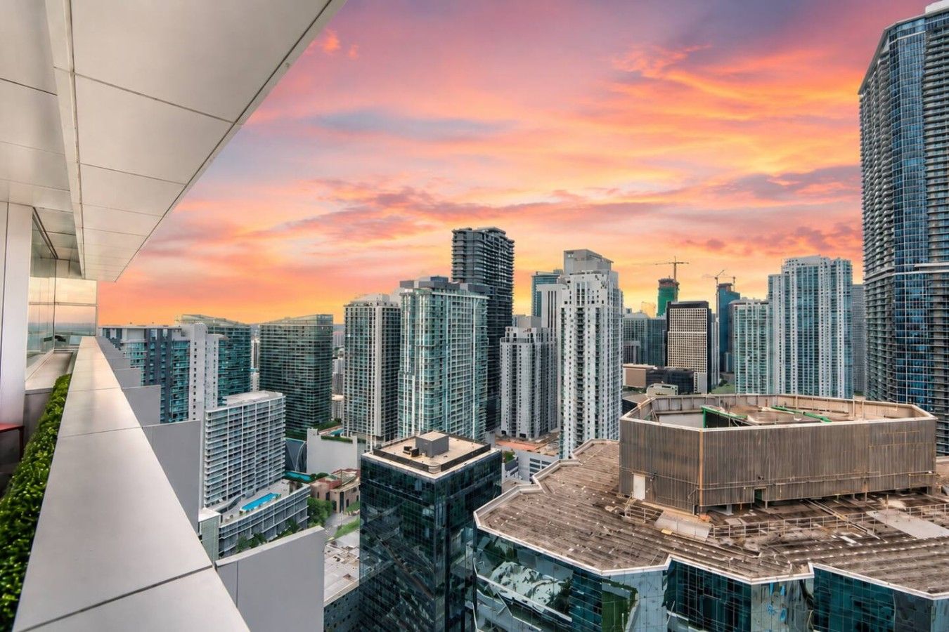 A high-rise building with a modern architectural design, featuring a rooftop pool and a view of a cityscape during sunset.