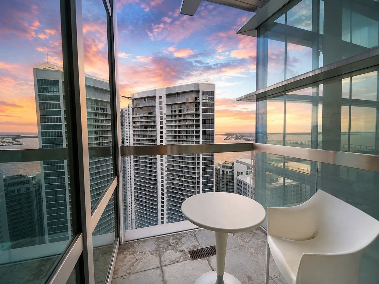 A high-rise building with a balcony, a round table, and a white chair.