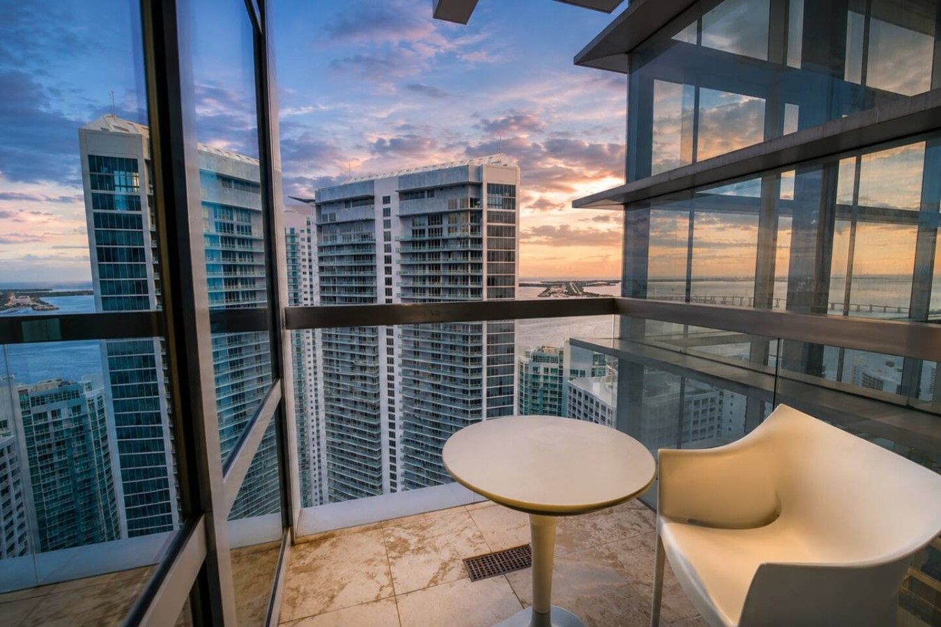 A high-rise building with a balcony, a round table, and a white chair.