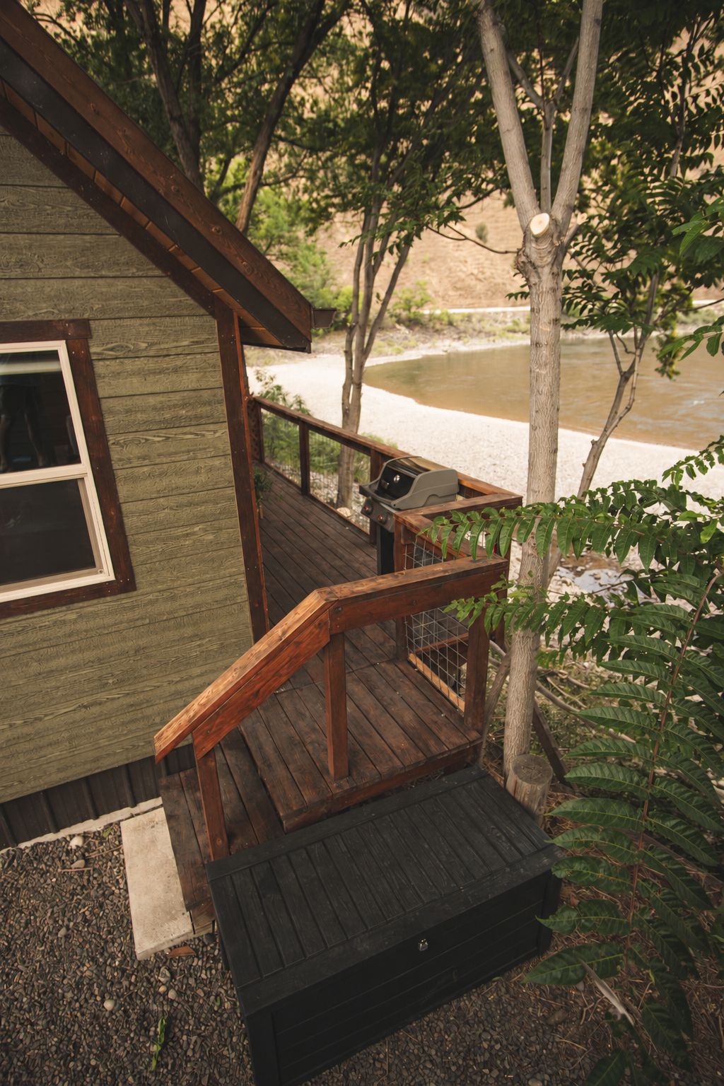 A wooden deck with a grill, a window, and a view of a body of water.