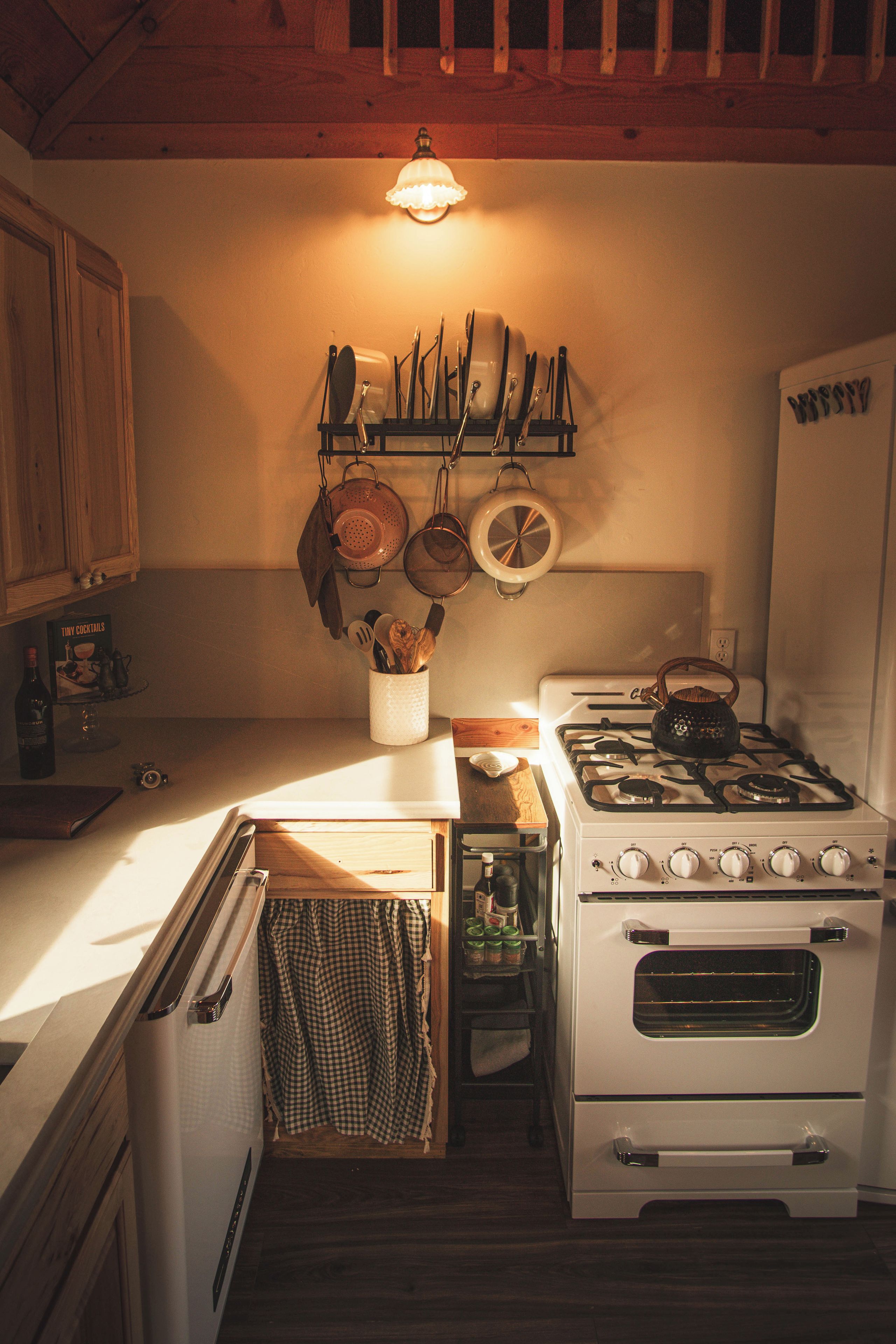 Cozinha compacta com fogão, forno e um suporte para panelas suspenso.