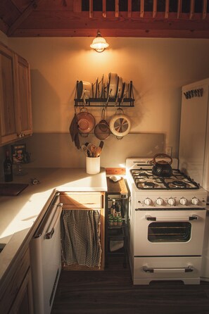 A compact kitchen with a stove, oven, and a hanging pot rack.