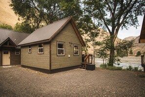 Une cabane en bois avec un toit en métal, une véranda et une vue sur la rivière.