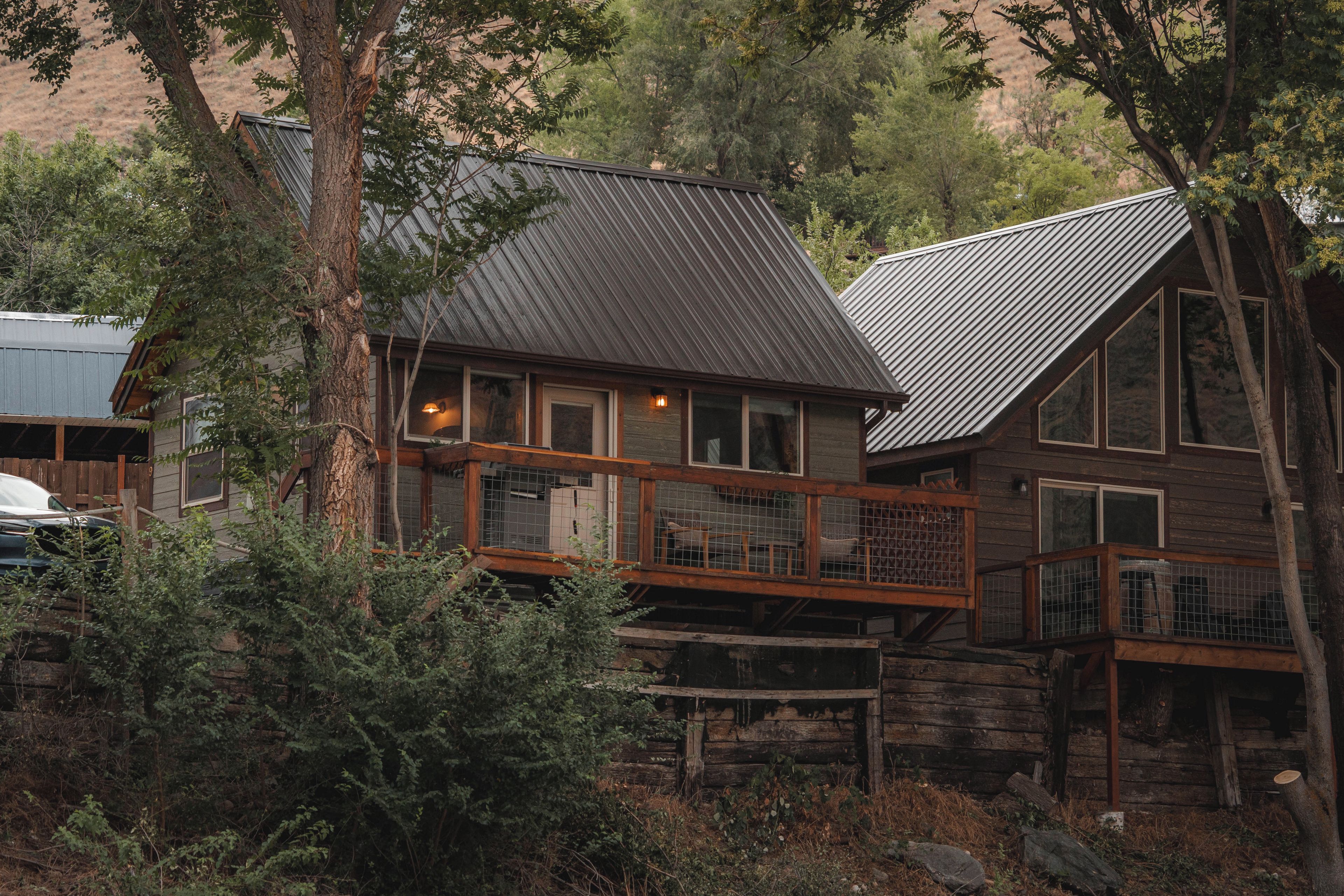 Une cabane rustique avec un toit en métal, une terrasse en bois et une véranda entourée d’une clôture.