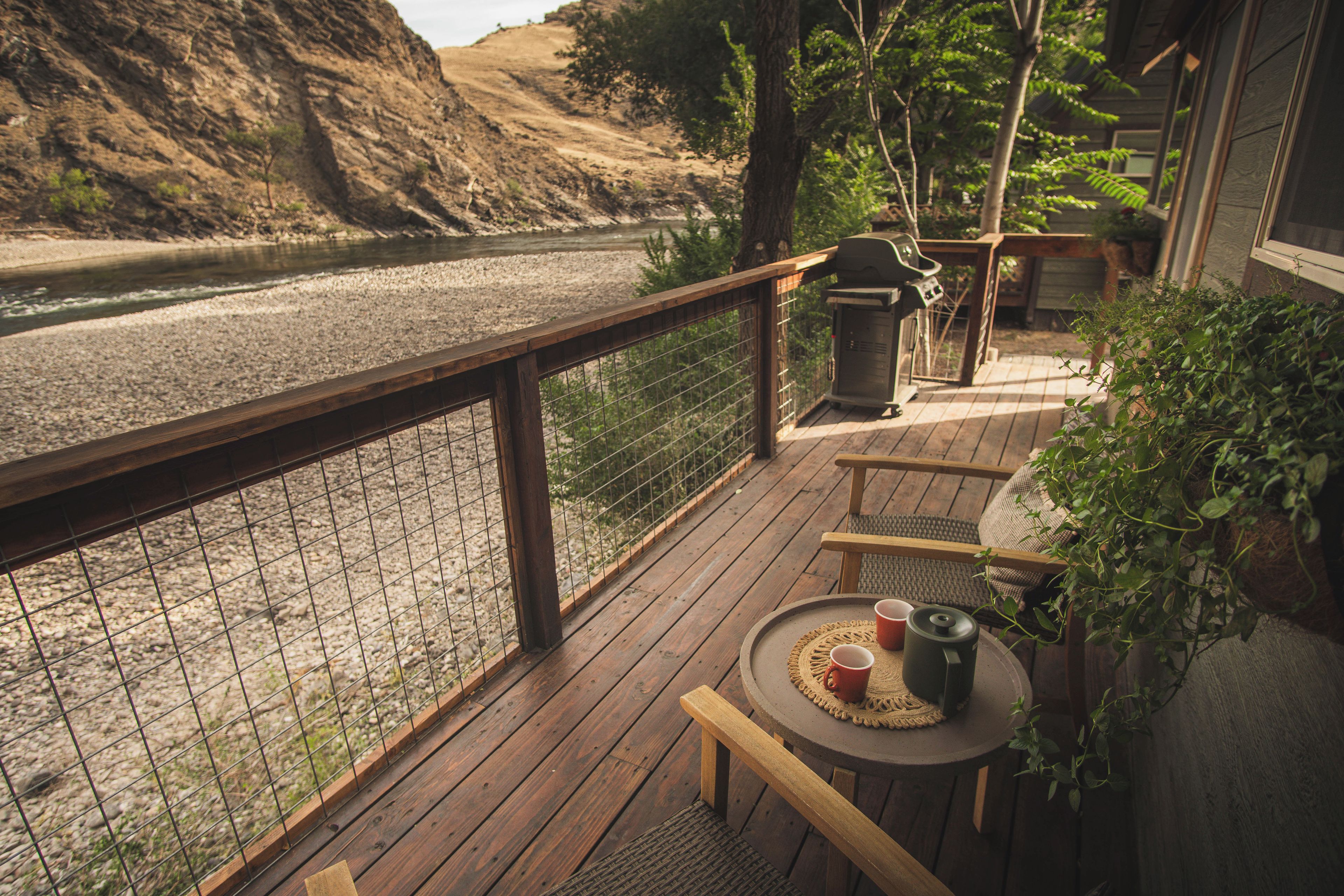 A wooden deck with a table and chairs, overlooking a river.