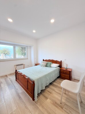 A bedroom with a wooden bed, a nightstand, a chair, and a window with a view of trees. - Beachfront home in Buarcos Beach! Perfect for families, pets, and groups! (Buarcos)