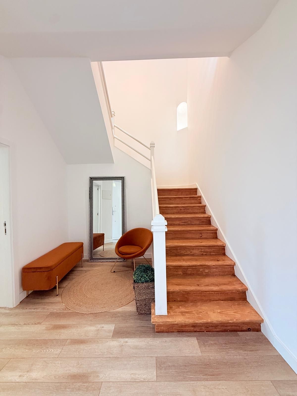Una escalera con peldaños de madera y balaustres blancos, que conduce a un piso superior.