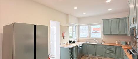 A spacious kitchen with a large refrigerator, wooden flooring, and light green cabinets.