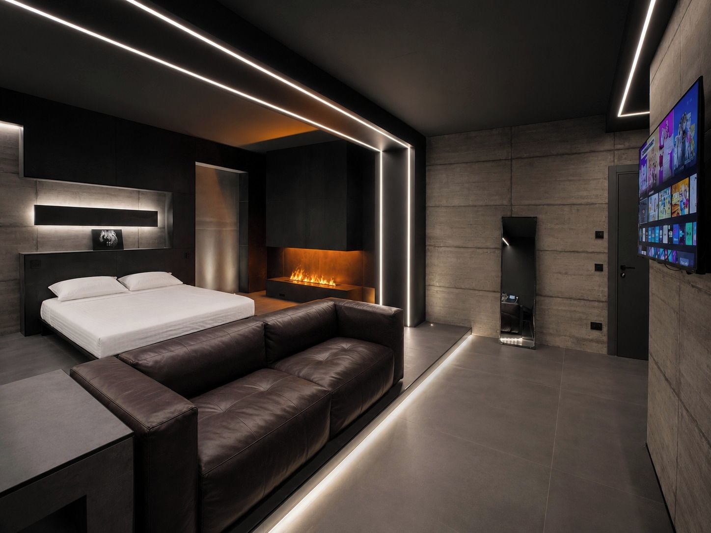 A modern bedroom with a bed, a leather sofa, a fireplace, and a TV mounted on the wall.
