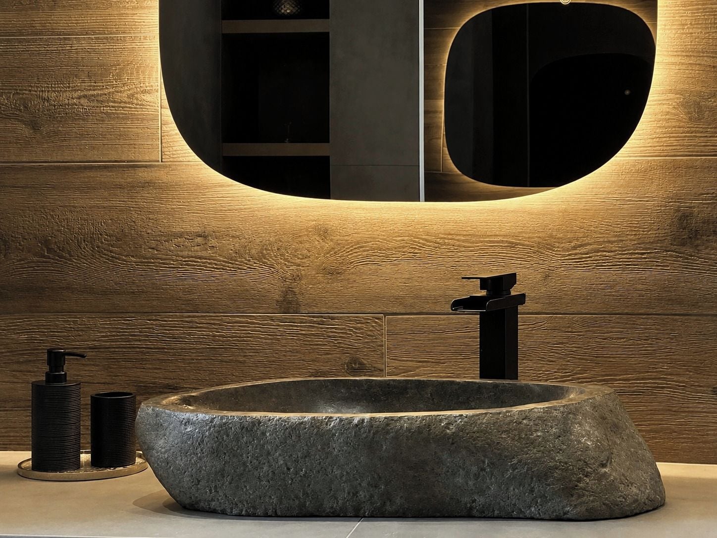A bathroom with a large, oval-shaped stone sink, a modern faucet, and a round mirror with a wooden frame.