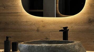 A bathroom with a large, oval-shaped stone sink, a modern faucet, and a round mirror with a wooden frame.