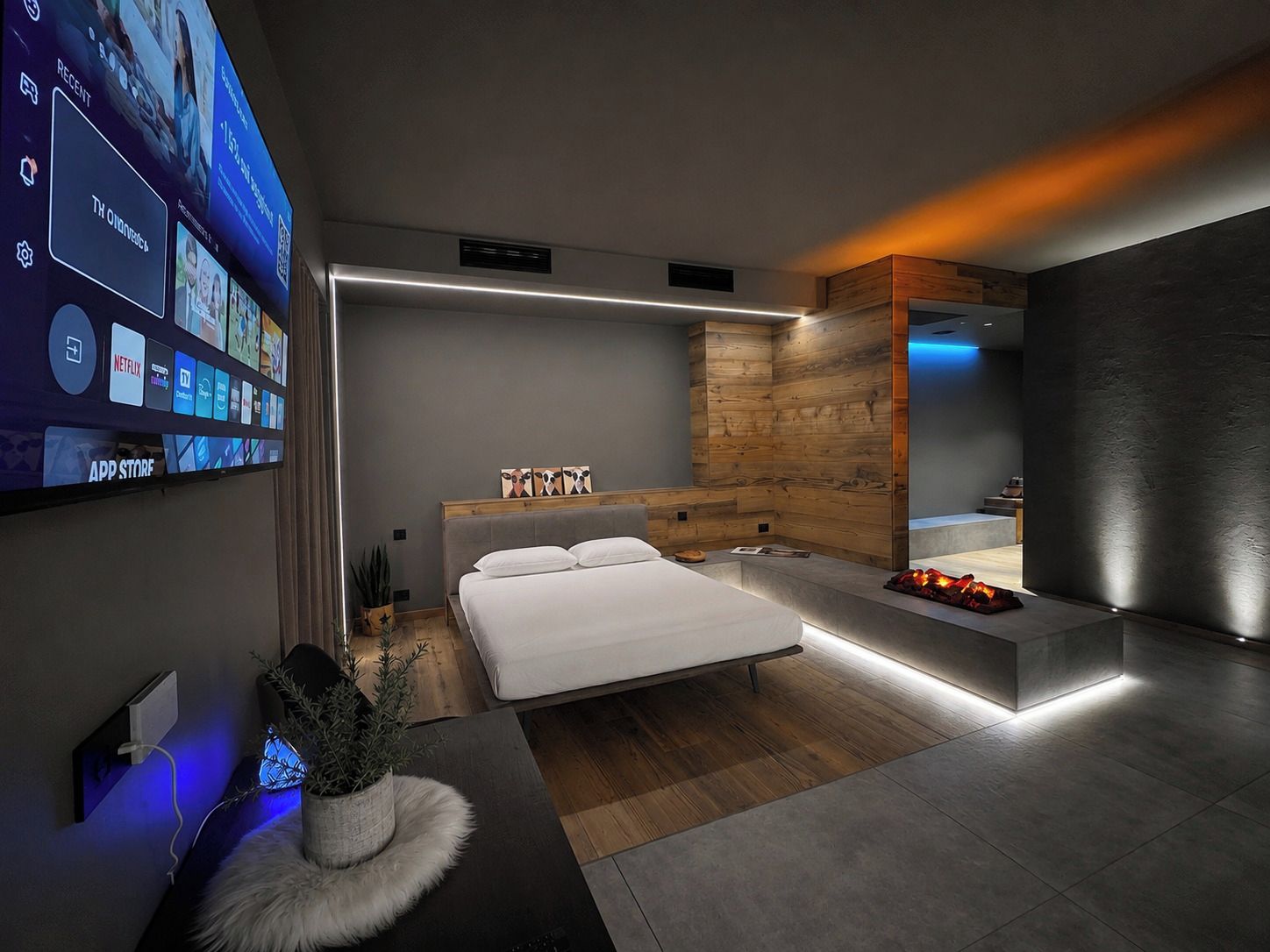 Une chambre moderne avec un grand lit, des tables de chevet, un banc intégré et un téléviseur fixé au mur qui affiche différentes applications.