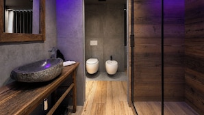 A modern bathroom with a stone sink, two toilets, and a wooden vanity. - Agarthi Suites (Piateda)
