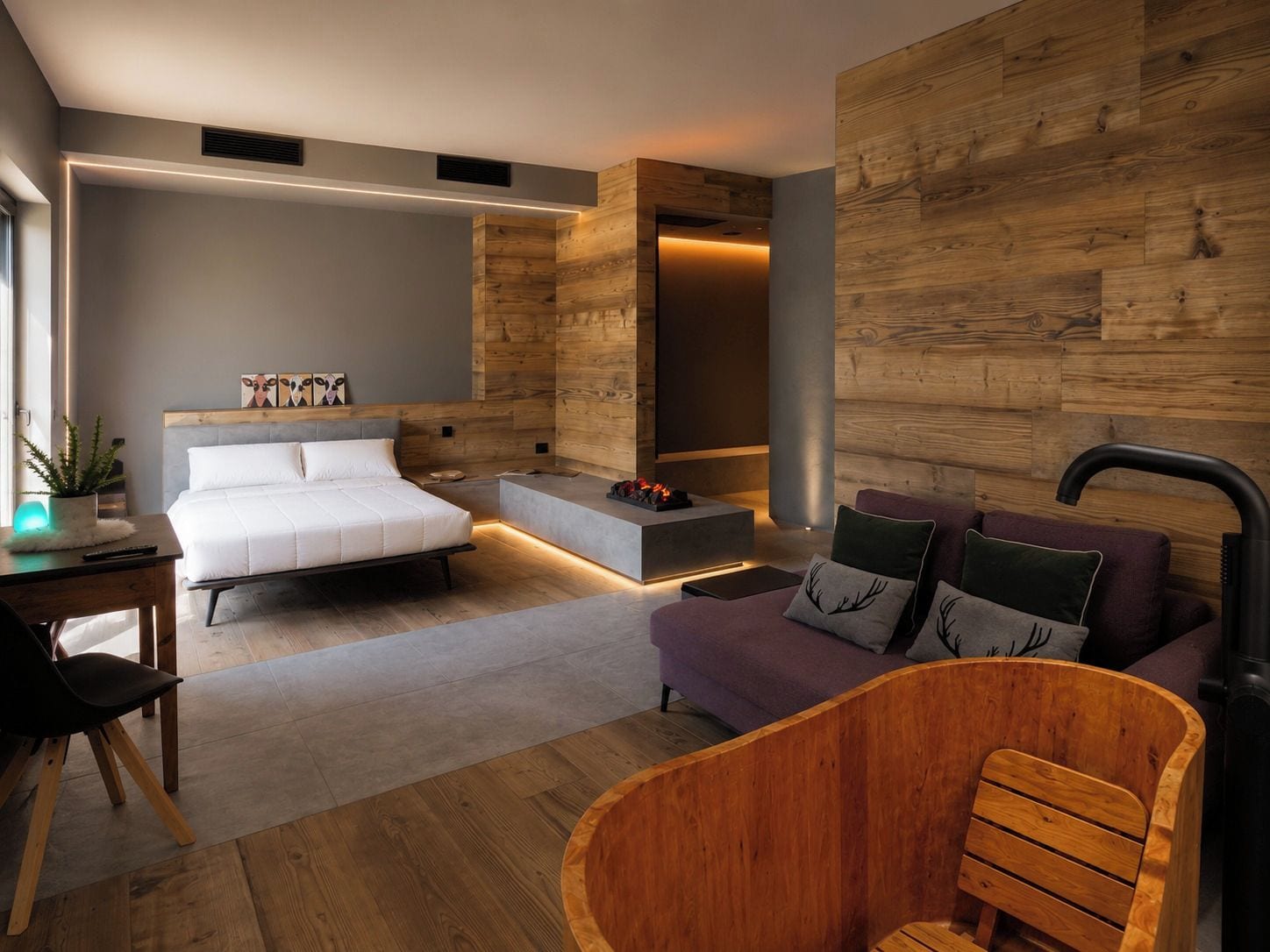 A modern bedroom with a bed, a sofa, a wooden bathtub, and a small table with a plant.