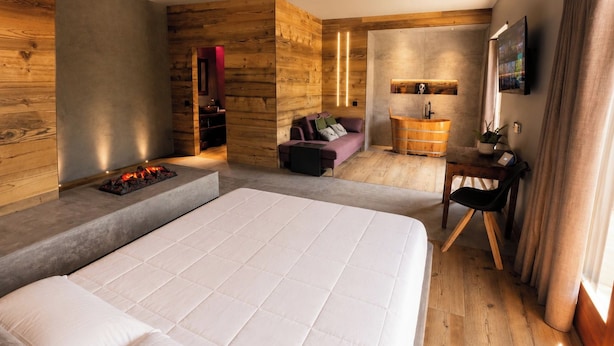 A modern hotel room with a large bed, a wooden accent wall, a small seating area, and a television. - Agarthi Suites (Piateda)