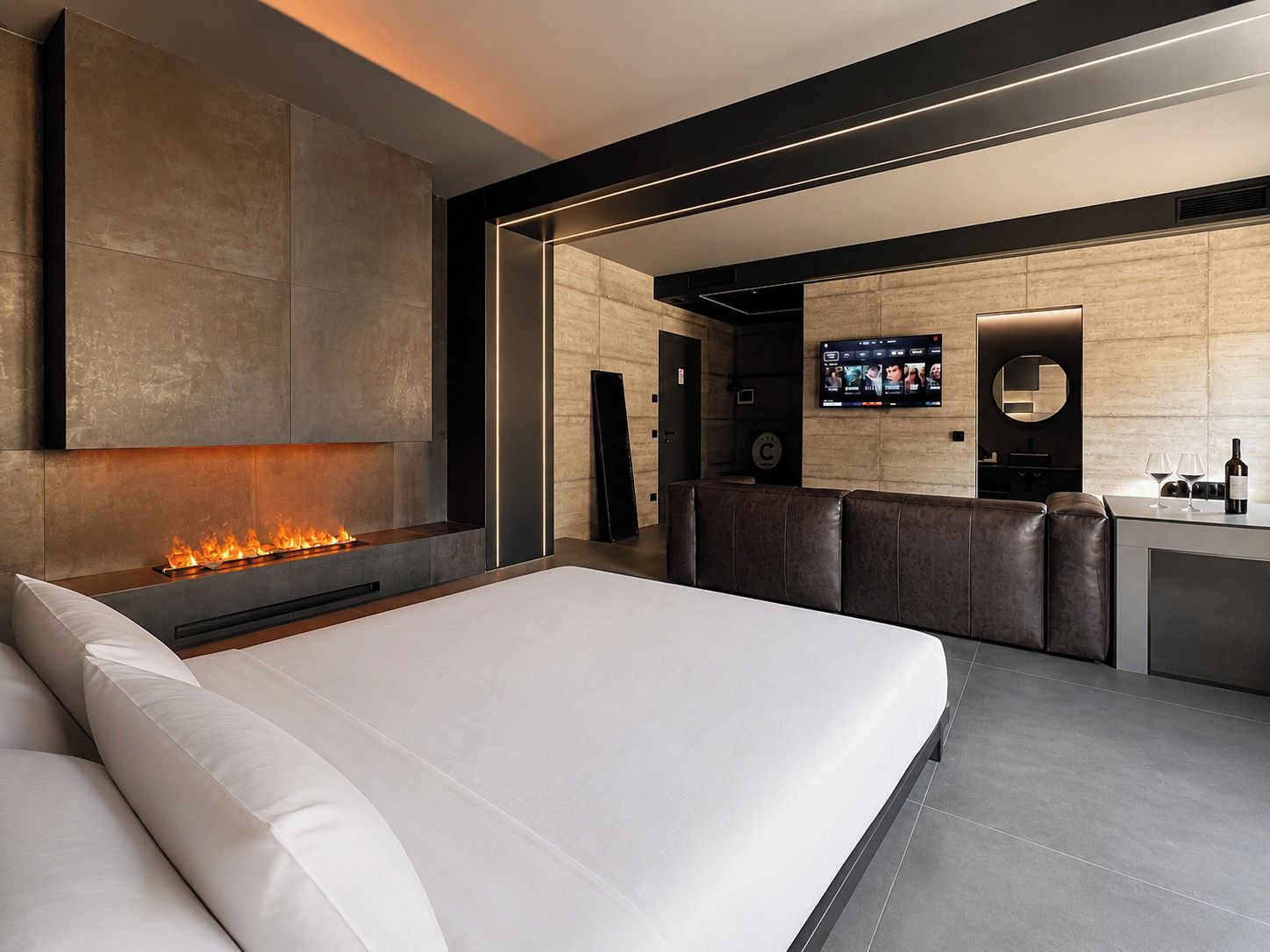 Een moderne hotelkamer met een groot bed, een open haard, een zithoek en een aan de muur bevestigde televisie.