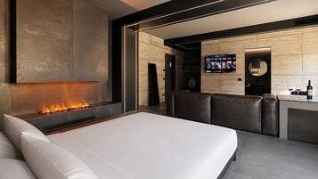 Een moderne hotelkamer met een groot bed, een open haard, een zithoek en een aan de muur bevestigde televisie.