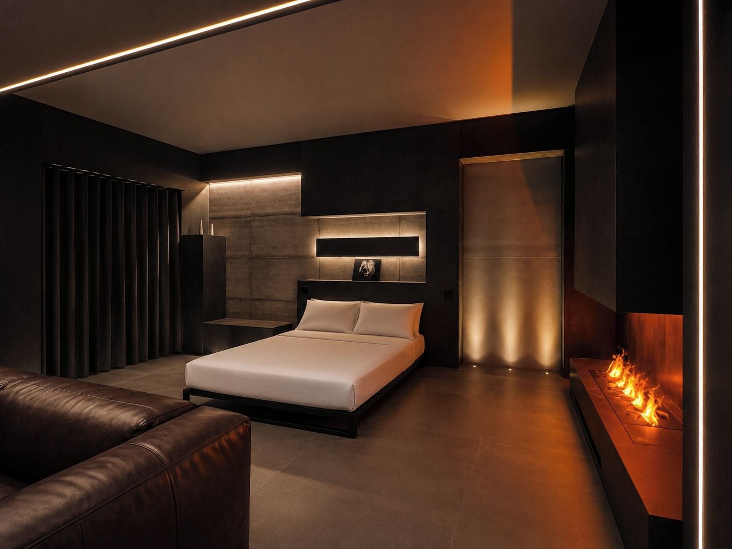 Ein modernes Schlafzimmer mit Bett, Sofa, Kamin und Wand-Fernseher.