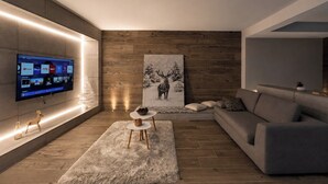 A modern living room with a flat-screen TV mounted on the wall, a large painting of a deer, a grey sofa, and a fluffy rug. - Agarthi Suites (Piateda)