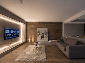 Uma sala de estar moderna com televisão de tela plana na parede, um quadro grande de um veado, um sofá cinza e um tapete fofo.