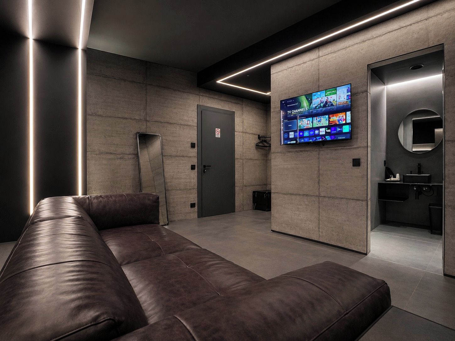 Eine moderne, minimalistische Lobby mit einer Ledersitzgruppe, einem digitalen Fernsehbildschirm und einem kleinen Badezimmer mit Spiegel und Waschbecken.